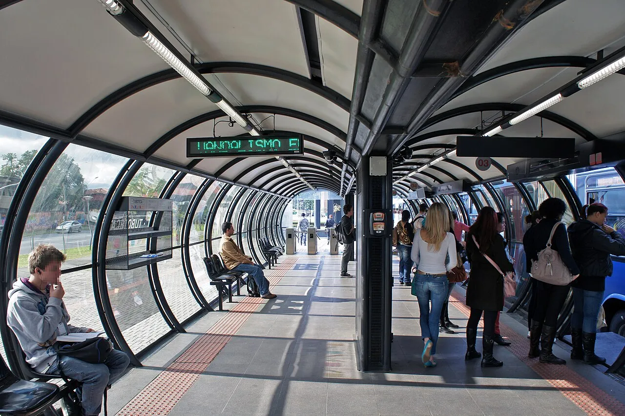 Interior de estação tubo da Linha Verde em Curitiba, com passageiros esperando e embarcando no ônibus biarticulado do sistema BRT