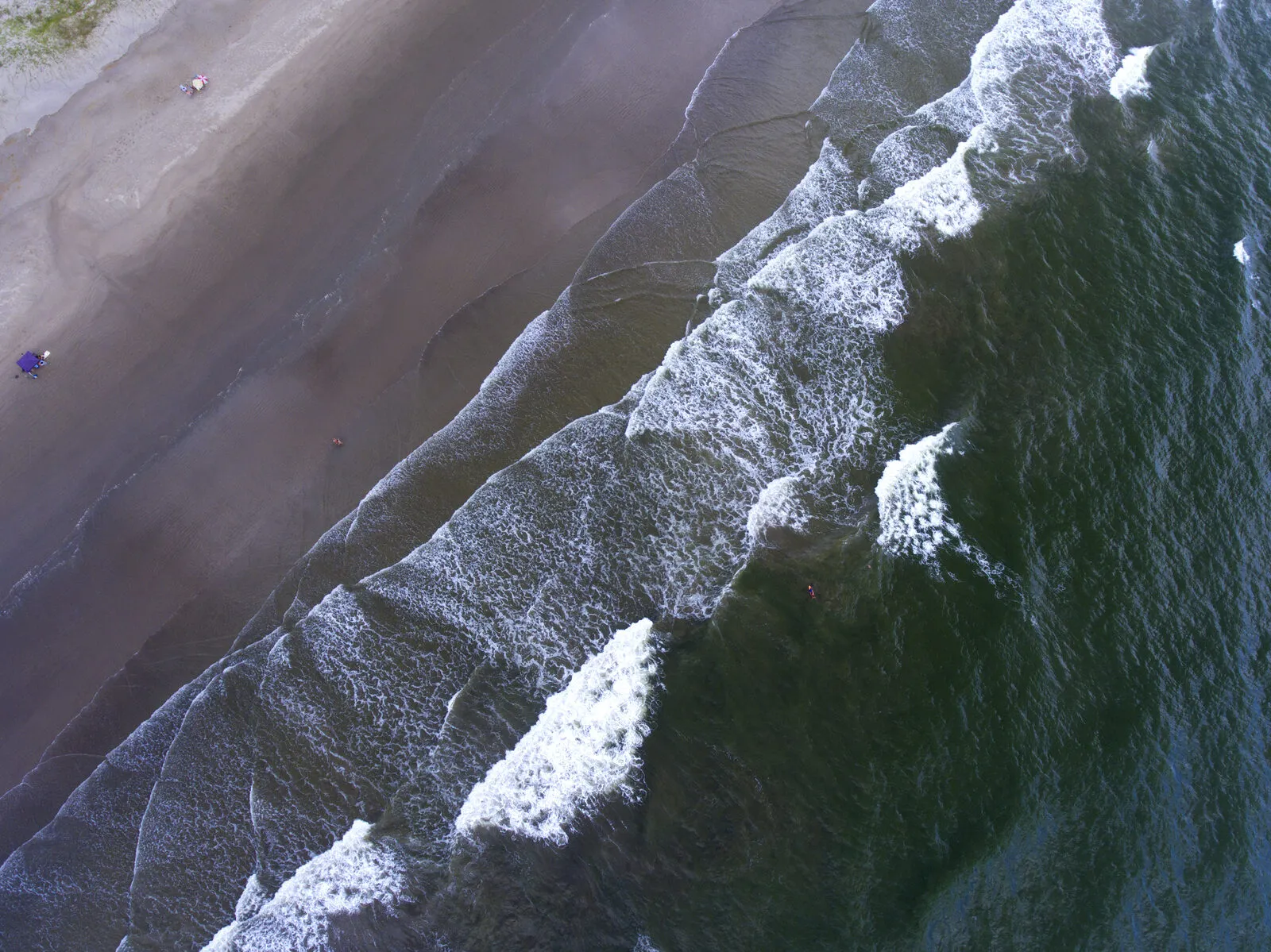 Vista aérea da Meia Praia, em Navegantes, com ondas se formando em faixas paralelas e um único banhista na areia