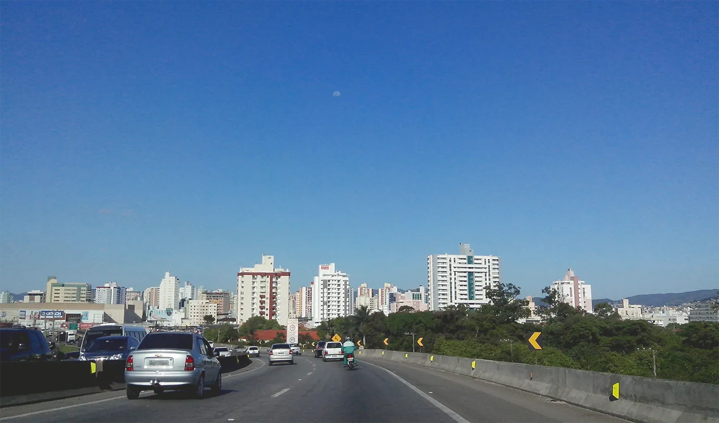 Vista do bairro Kobrasol, em São José, SC, a partir da BR-101, com prédios altos ao fundo e fluxo de veículos em primeiro plano