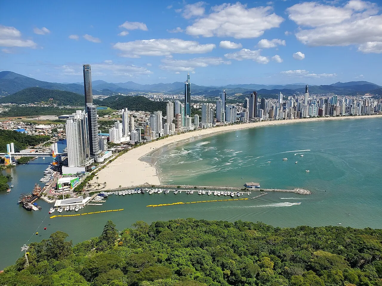 Vista aérea da orla de Balneário Camboriú a partir do Parque Unipraias, com a faixa de areia alargada e os arranha-céus da Avenida Atlântica ao fundo